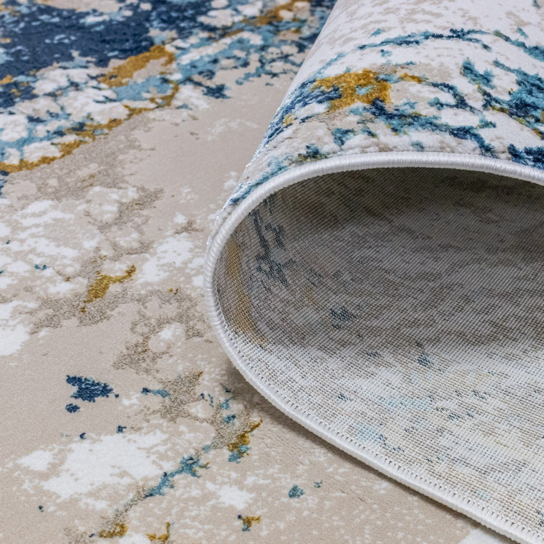 Paradise Living – Tapete Batik 38/004 Azul, detalhe da base antiderrapante e acabamento do rebordo, padrão abstrato azul e dourado
