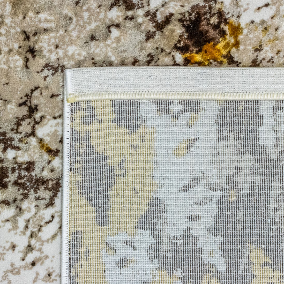 Paradise Living – Tapete Batik 38/008 Castanho, detalhe do canto com verso resistente ao desgaste e costura de rebordo, padrão castanho e dourado visível