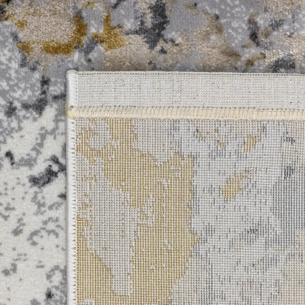 Paradise Living – Tapete Batik 38/017 Cinzento, detalhe do canto com verso resistente ao desgaste e costura de rebordo dupla, padrão cinzento e dourado visível