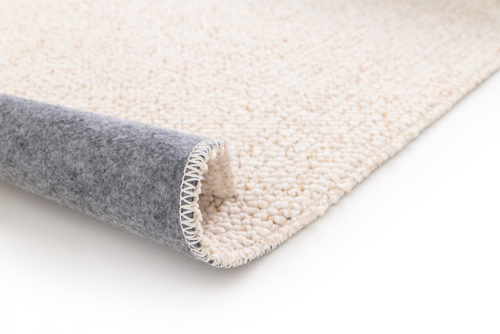 Paradise Living – Tapete Polo 71511/056 Bege Creme perspetiva do canto dobrado mostrando textura de lã grossa creme e verso em feltro cinzento