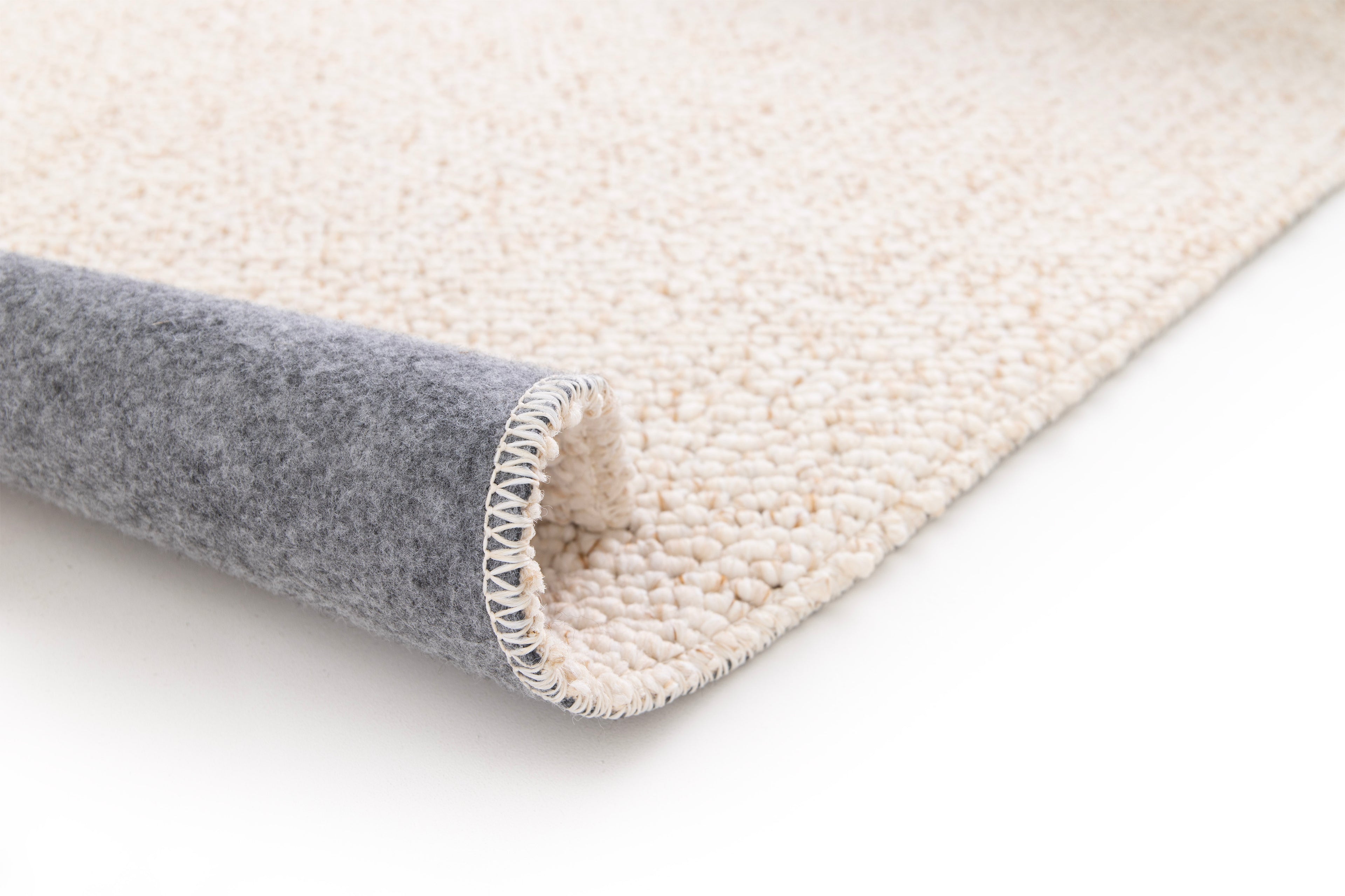 Paradise Living – Tapete Polo 71511/056 Bege Creme perspetiva do canto dobrado mostrando textura de lã grossa creme e verso em feltro cinzento