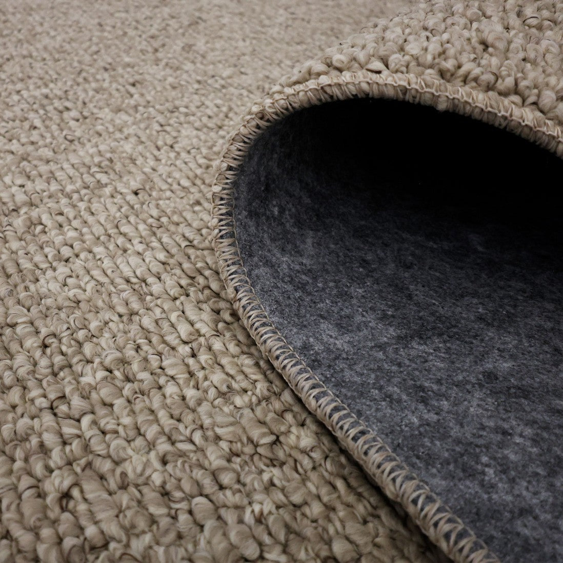 Paradise Living – Tapete Bhutan 71591/056 Bege detalhe do canto enrolado mostrando textura bouclé bege e verso em feltro cinzento antiderrapante
