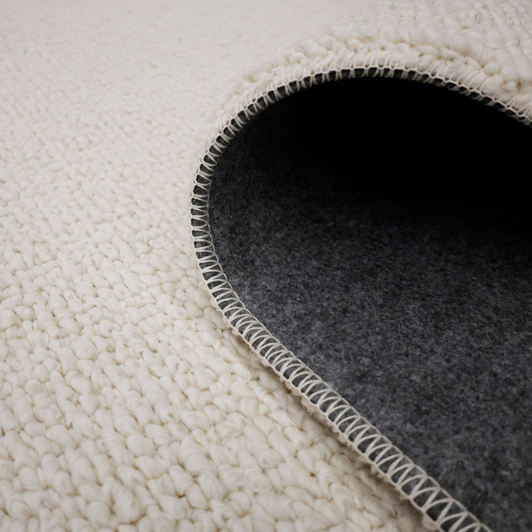 Paradise Living – Tapete Bhutan 71591/066 Branco close-up do canto enrolado mostrando textura bouclé branca e verso em feltro cinzento antiderrapante