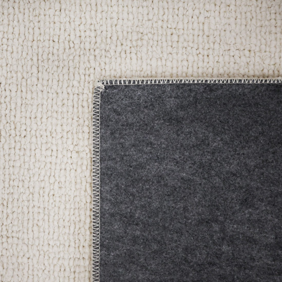 Paradise Living – Tapete Bhutan 71591/066 Branco detalhe do canto dobrado mostrando frente em bouclé branco e verso em feltro cinzento escuro
