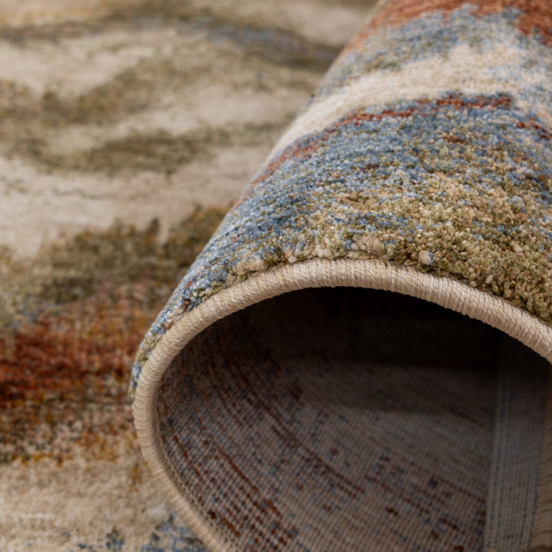 Paradise Living – Tapete Odense 7435/192 close-up do verso enrolado com orla em bege e textura multicolor em tons azul, terracota e castanho