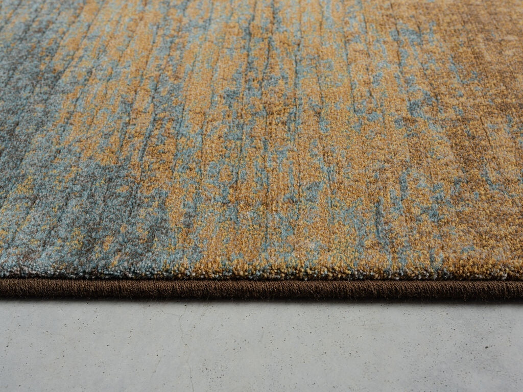 Paradise Living – Tapete Giacomo 63029/1219 detalhe da orla lateral com textura densa em tons castanho dourado e azul acinzentado intercalados